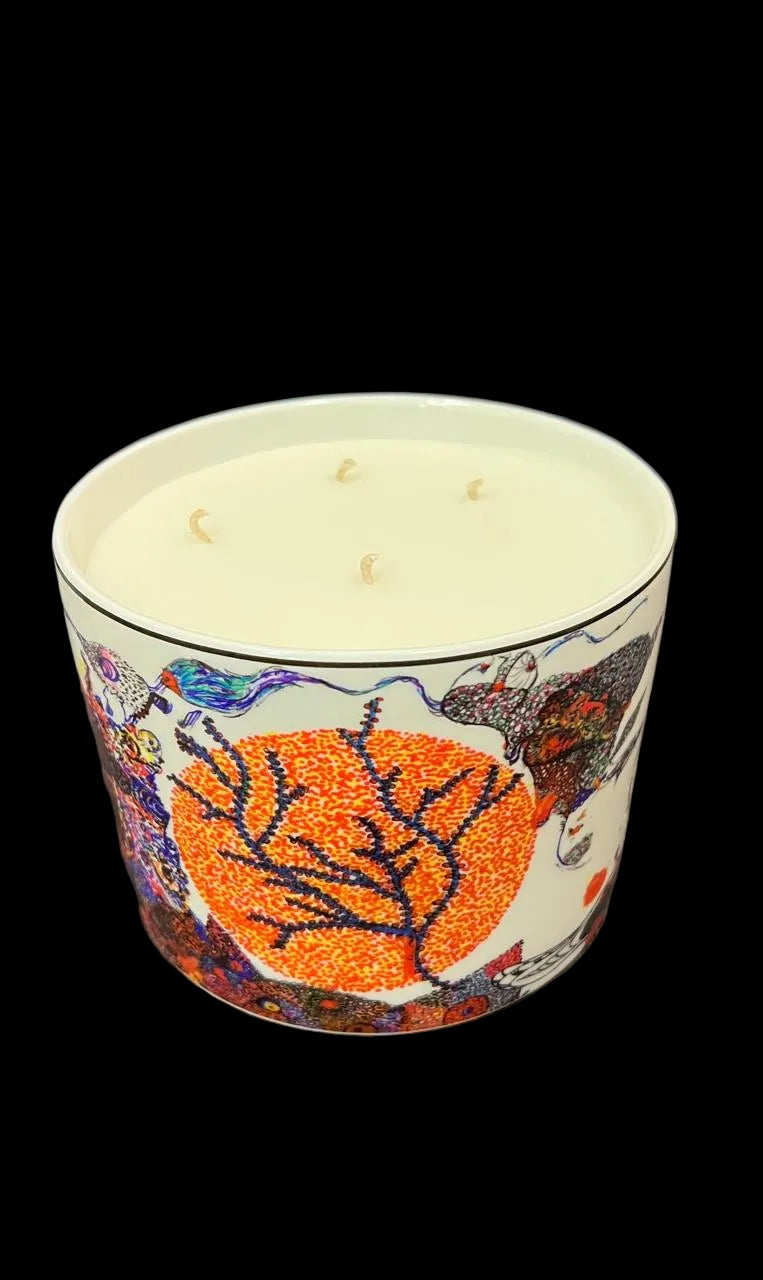A three-wick scented candle in a white ceramic pot with a colorful, textured graphic design featuring a prominent orange leaf motif, set against a dark gray textured fabric background.