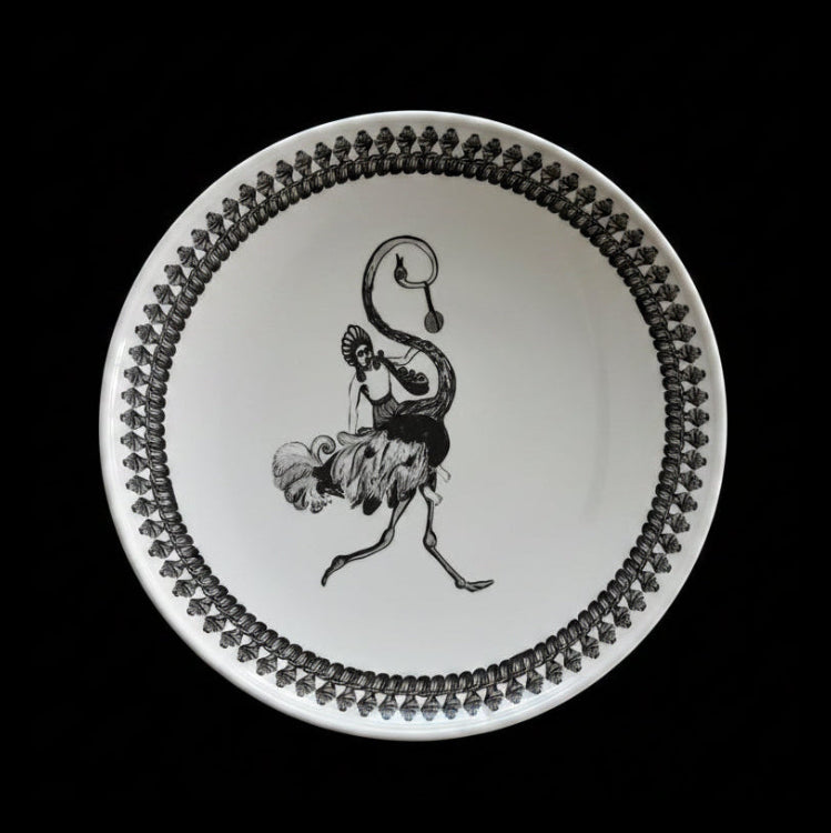 A white ceramic plate featuring a black illustration of a dancing figure in the center and a decorative border of repeating black teardrop shapes around the rim, shown against a solid black background.
