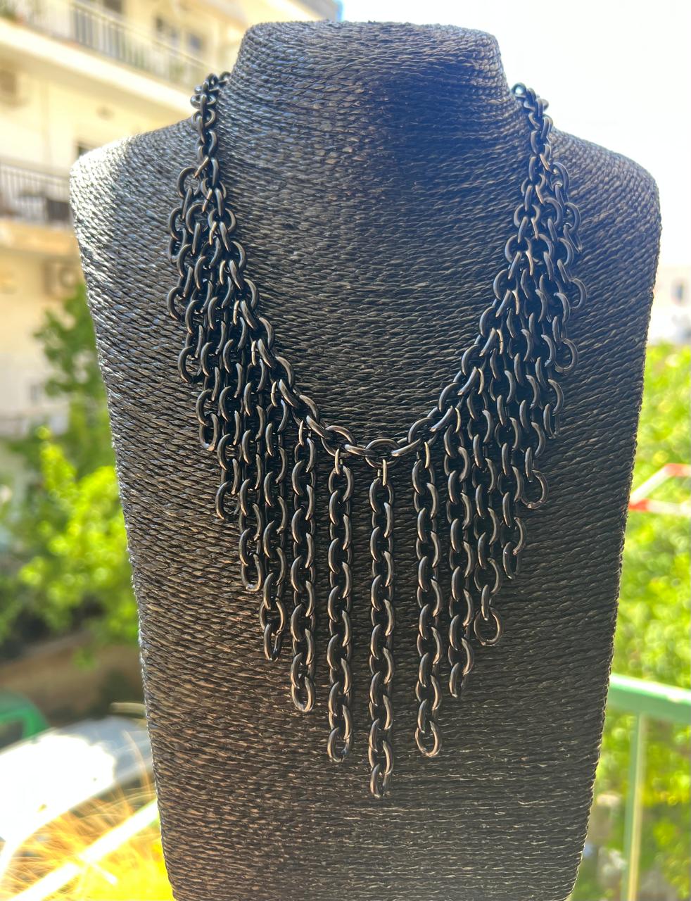 A dark metallic multi-strand chain necklace displayed on a black textured mannequin bust