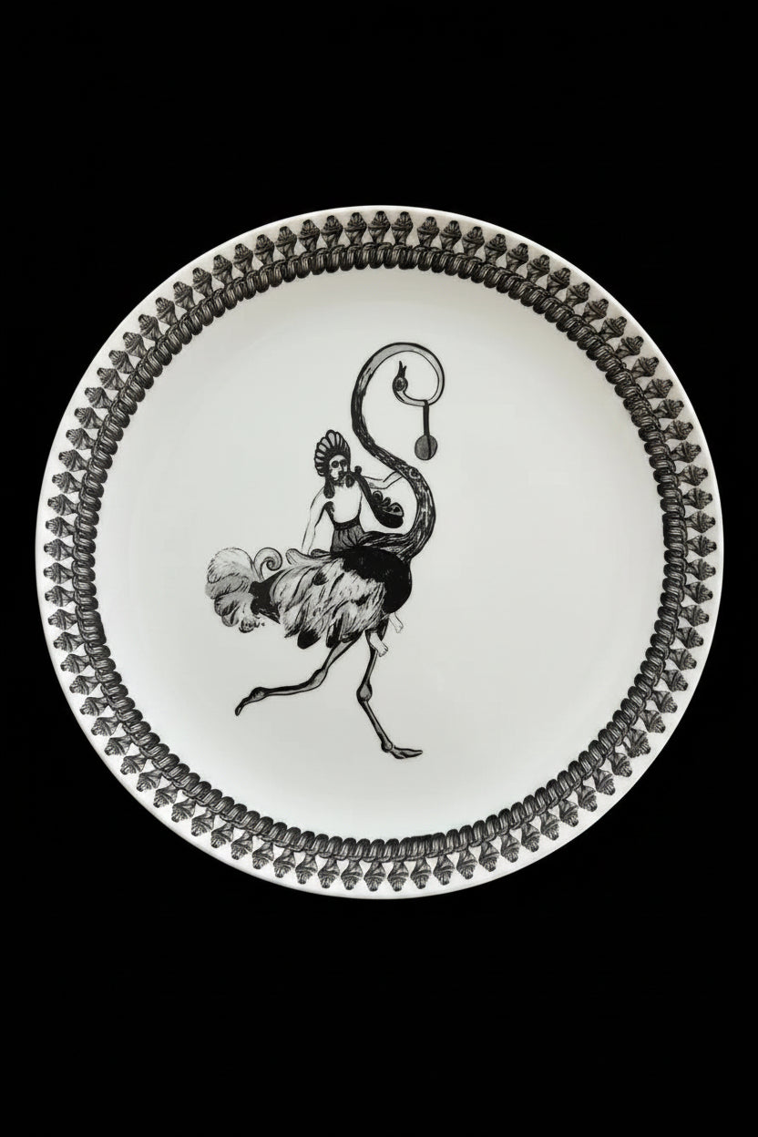 A white ceramic plate with a black line-art illustration of a woman riding an ostrich, placed on top of a square black and white patterned tray.